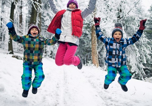 Three people jumping joyfully in a snowy forest, dressed in colorful winter clothing and surrounded by snow-covered trees.