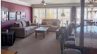 Cozy living room with purple accent wall, L-shaped sofa, coffee table, reclining chair, and a row of bar stools along a counter by large windows.