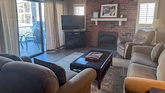 Cozy living room with a brick fireplace, brick accent wall, large sofa set, coffee table, TV on a stand, and sliding glass doors to a balcony.