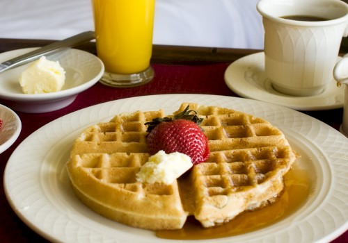 A breakfast scene: waffles with butter and syrup, strawberries, orange juice, coffee, and a cozy bed backdrop. Ending punctuation.