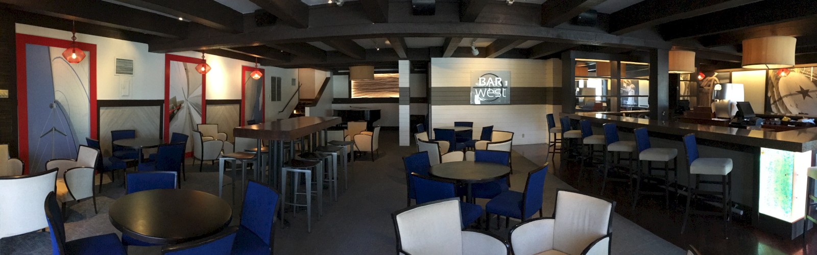 The image shows an interior of a modern bar with a variety of seating including chairs and bar stools, and a counter on the right side.