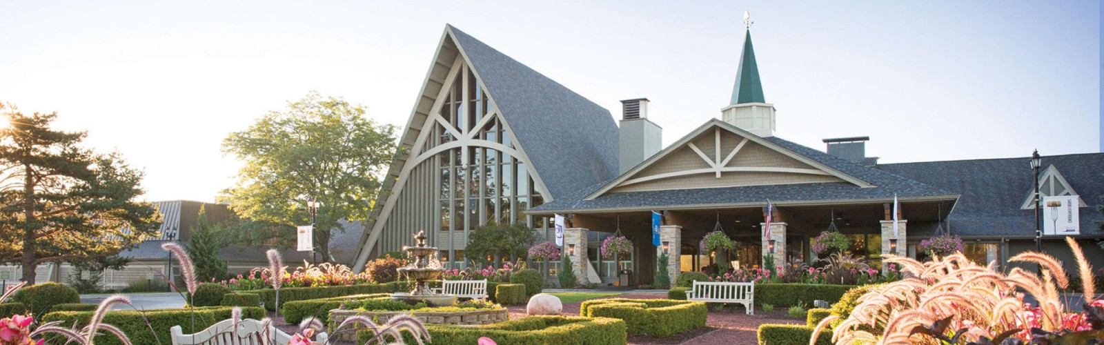 A charming building with a tall triangular roof, surrounded by lush gardens and vibrant flowers, under a clear sky during daylight.