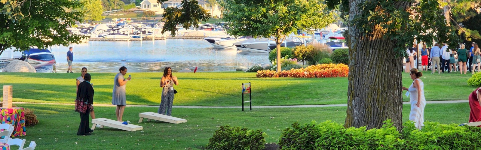 People are enjoying a lakeside gathering with various activities, including playing games and socializing on a lush green lawn.