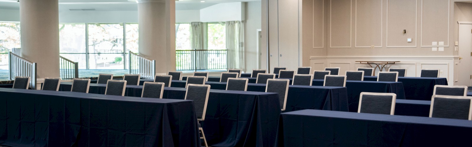 An empty conference room with rows of tables and chairs arranged neatly, under elegant ceiling lights.