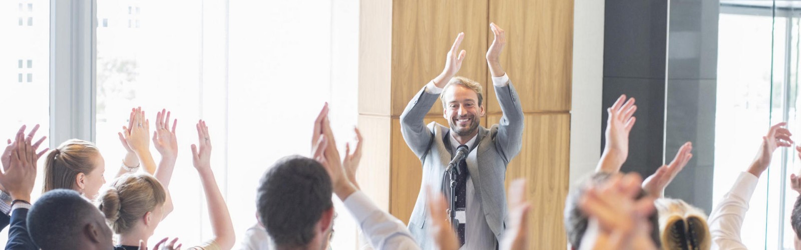A group of people are standing and clapping with their hands raised while a man in the front leads the activity, also clapping with a smile.