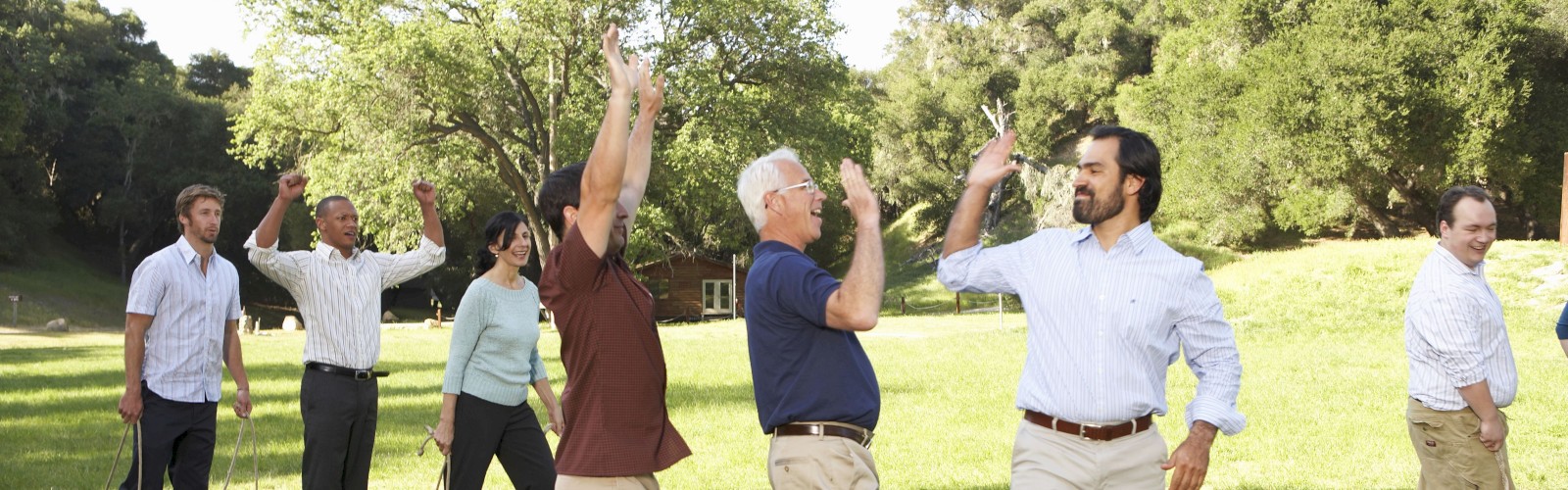A group of people appears to be having fun outdoors, giving high-fives in a park-like setting with trees in the background.