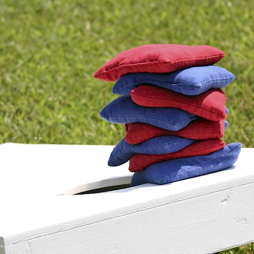 A stack of red and blue cushions is arranged on a white bench outdoors near green grass, creating a colorful and cozy display.