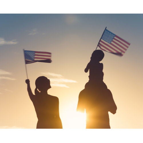 A silhouette of a person holding two American flags, with a child sitting on someone’s shoulders at sunset.