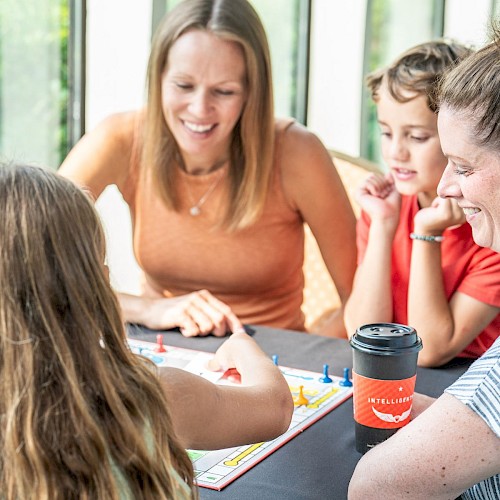 A woman and two children are playing a game of Monopoly while smiling and enjoying each other's company at a table.