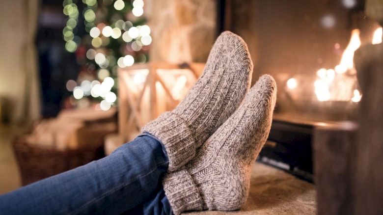 Person relaxing by a cozy fireplace during Christmas, with festive lights and decorated tree in the background.