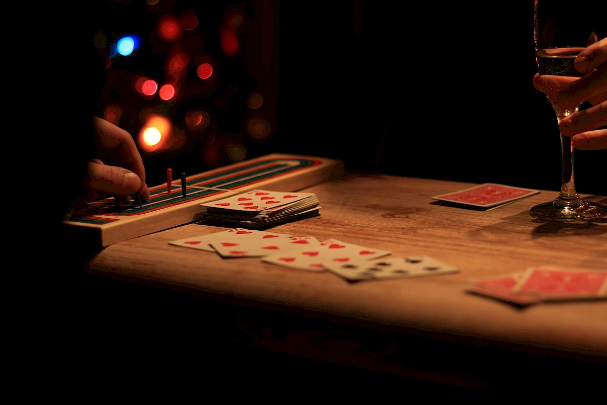 People playing a card game at a wooden table with a glass of champagne, illuminated by dim, warm lighting.