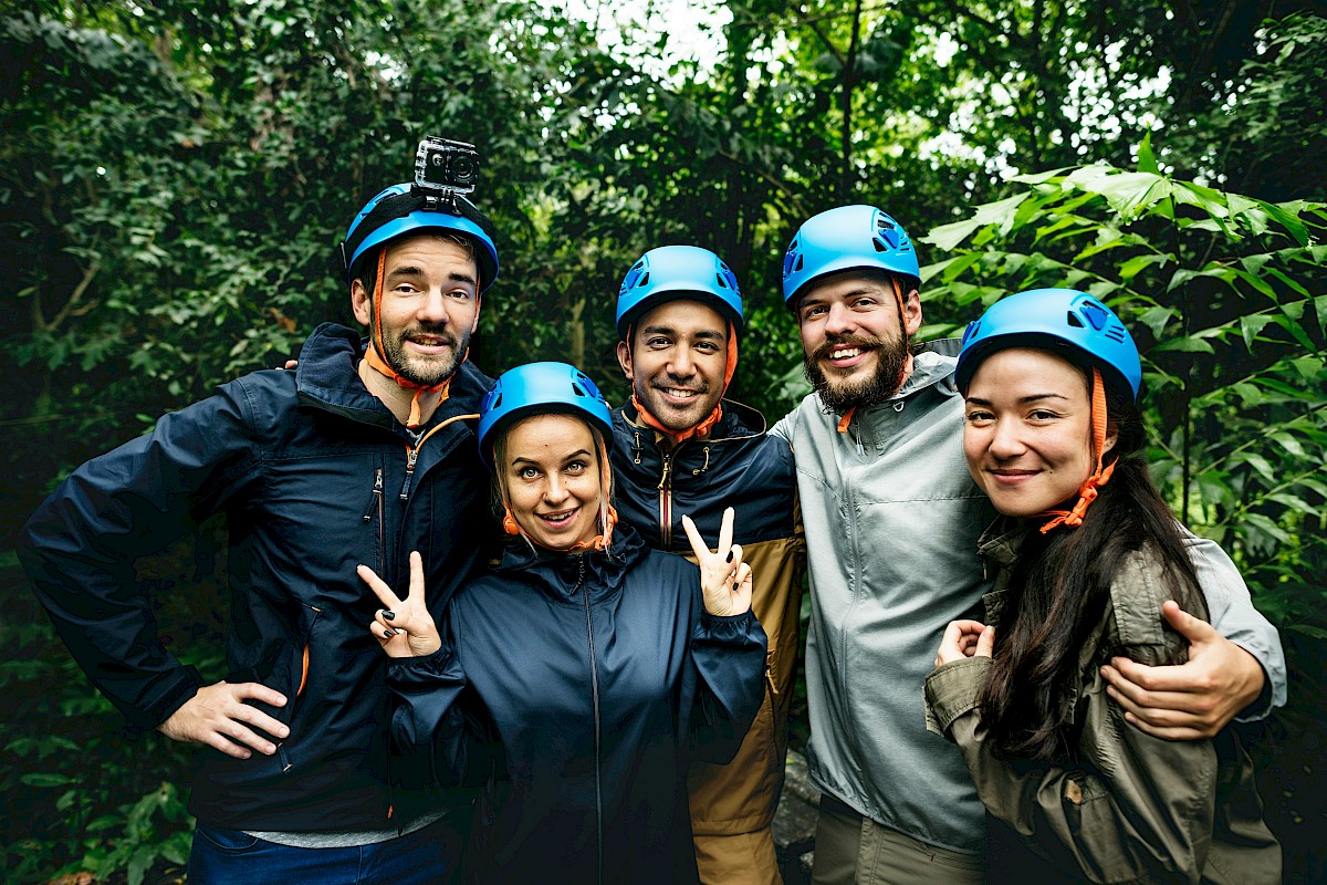 Group of five friends wearing helmets, smiling, and posing in a lush, green outdoor forest setting.