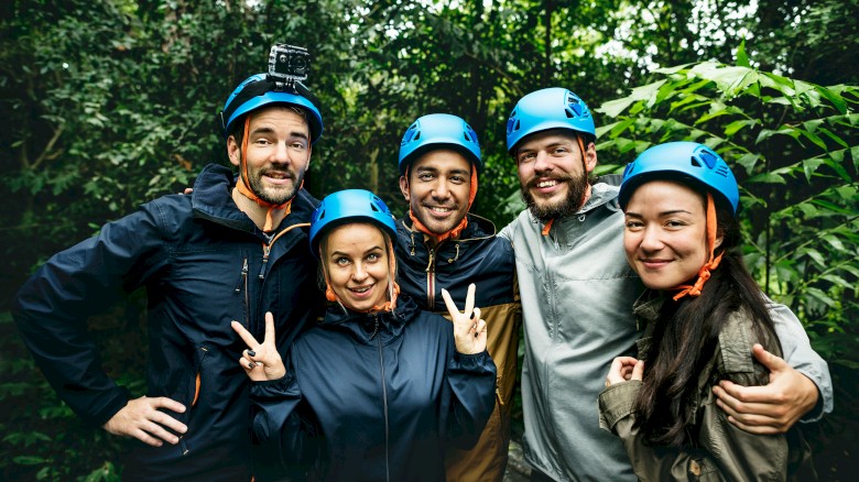 Group of five friends wearing helmets, smiling, and posing in a lush, green outdoor forest setting.