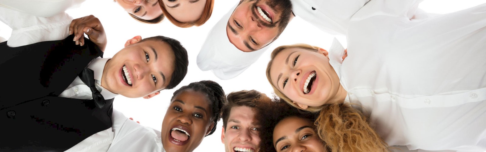 A group of eight cheerful people dressed in uniforms, standing in a circle and looking down at the camera, smiling widely.