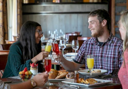 A group of people enjoying a meal at a restaurant, sharing a toast with drinks, surrounded by plates of food and desserts, and smiling warmly.