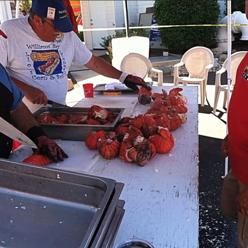 Three men prepare and cook pumpkins outdoors, with one slicing, another cutting, and a third overseeing the pumpkin pile on the table.