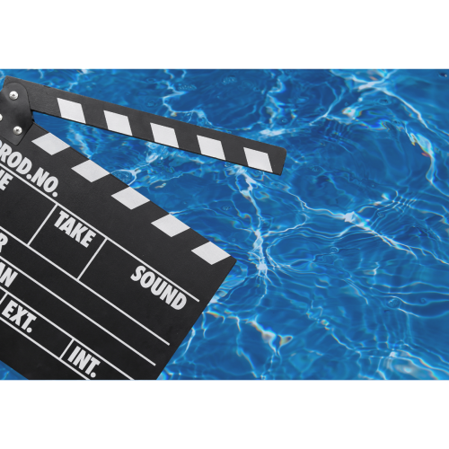 A film clapperboard is floating on a blue, rippling water surface, likely on a swimming pool.