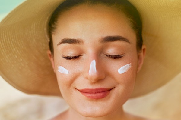 A woman with a big straw hat on her head, smiling with closed eyes, and sunscreen on her nose and cheeks.