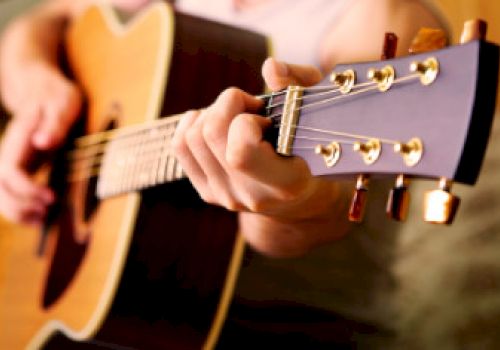 A person is playing an acoustic guitar, focusing on the fretboard and strings. The image captures the hand positioning and details of the instrument.