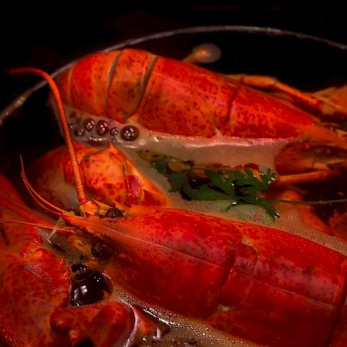 The image shows a dish with cooked lobsters in a sauce, garnished with herbs and served in a bowl.