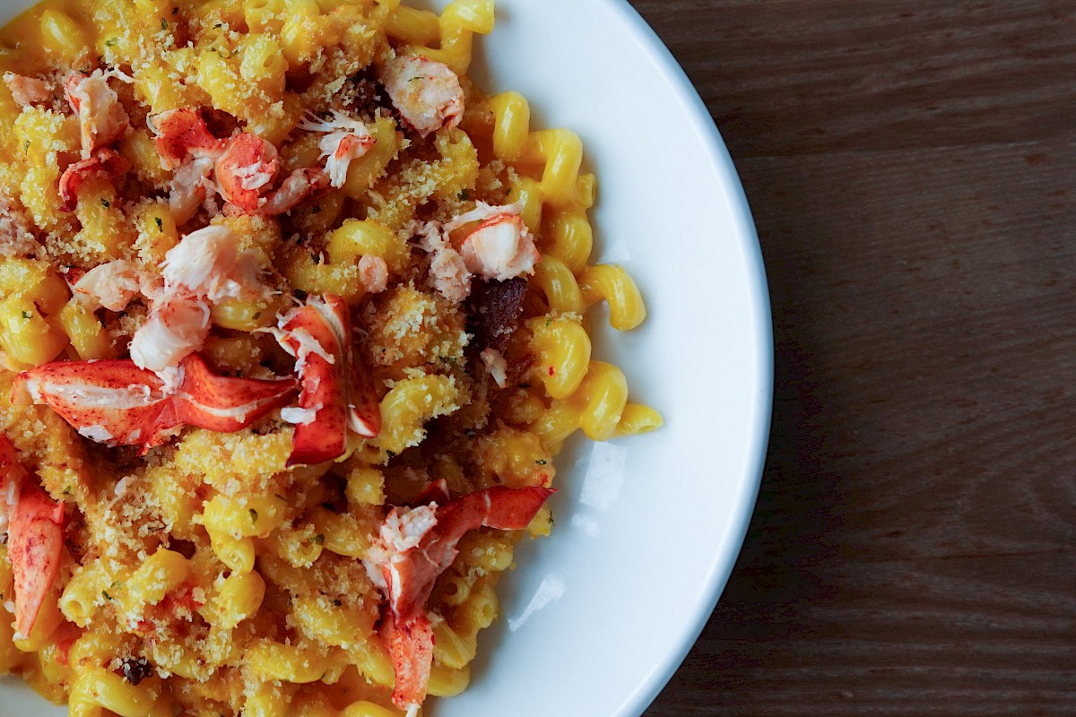 A plate of pasta with lobster and a crumbly topping, served on a white dish against a wooden table background.