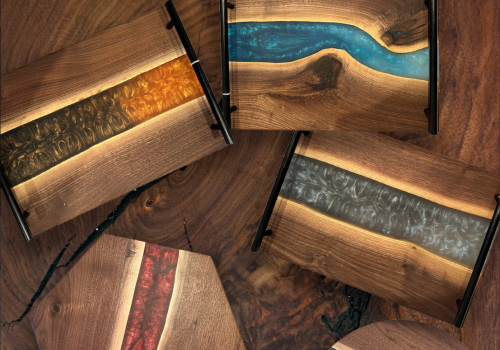 This image features five wooden trays with colorful resin inlays in various patterns, laying on top of a wooden surface.
