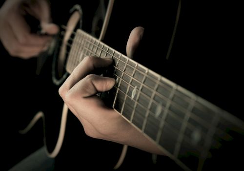A close-up shot of a person playing an acoustic guitar, focusing on their hands on the fretboard and strumming the strings.