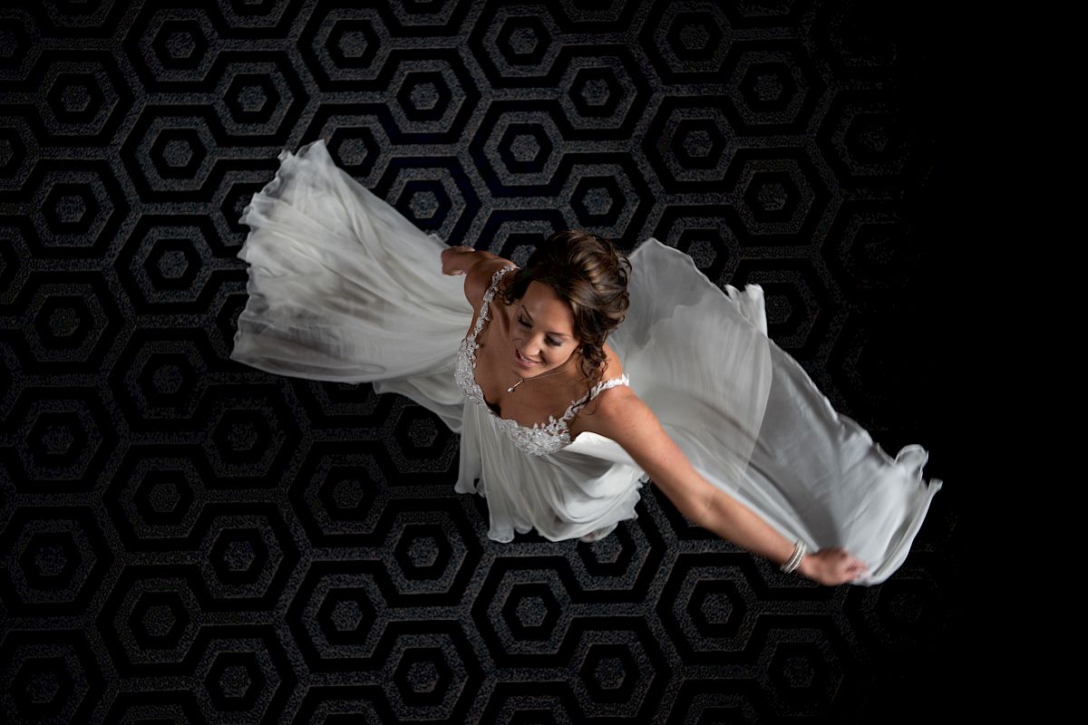 A woman in a white dress is dancing, captured from above, with a dark hexagonal patterned floor as the background.