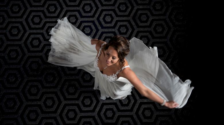 A woman in a white dress is dancing, captured from above, with a dark hexagonal patterned floor as the background.