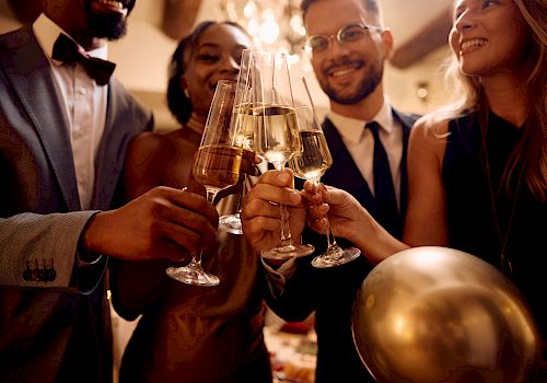 A group of people dressed elegantly are toasting with champagne glasses at a celebration, one person holding a gold balloon in their hand.