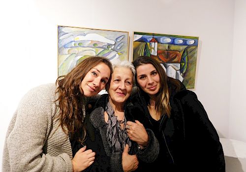 Three people are standing close together in front of two abstract paintings, smiling at the camera.