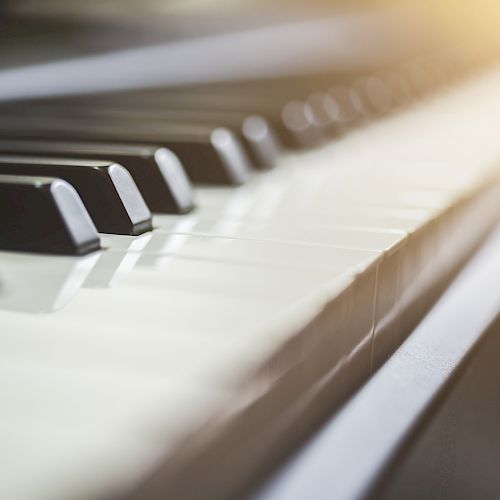 This image shows a close-up of piano keys with sunlight softly illuminating the keys, creating a serene and artistic atmosphere.