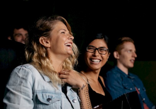 Three people are seated, smiling and laughing, as they enjoy some kind of show or event.