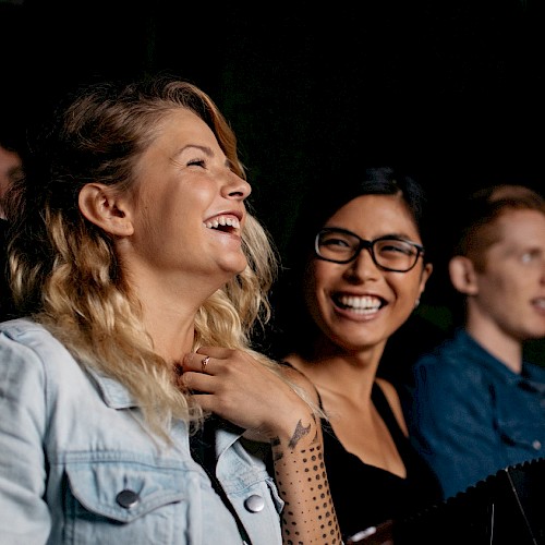 Three people are sitting and laughing, likely enjoying a movie or performance together.