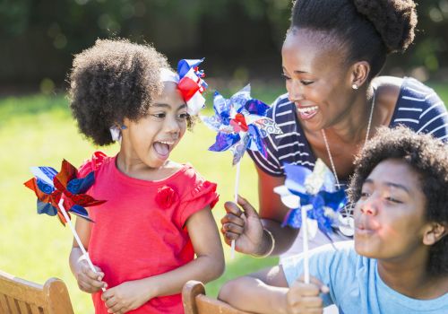 A joyful group of three people play outdoors with colorful pinwheels, enjoying their time together in a sunny park setting.