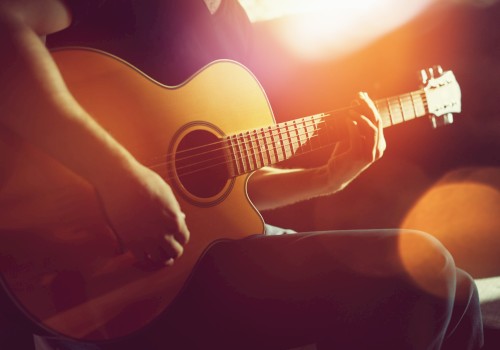 A person is playing an acoustic guitar in a warmly lit setting, with a focus on their hands on the strings.