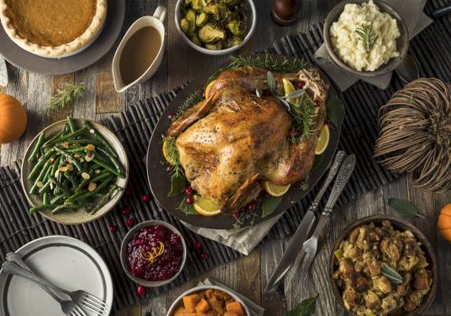 A table is set with a roasted turkey, mashed potatoes, green beans, stuffing, cranberry sauce, sweet potatoes, gravy, pie, and various vegetables.