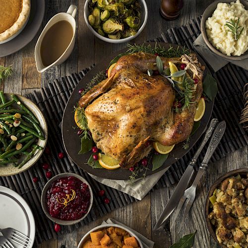 A table is set with a roasted turkey, mashed potatoes, green beans, stuffing, cranberry sauce, sweet potatoes, gravy, pie, and various vegetables.