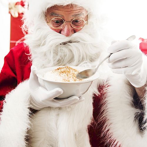 An individual dressed as Santa Claus is holding a bowl and eating with a spoon, appearing to be enjoying a meal, likely porridge or soup.
