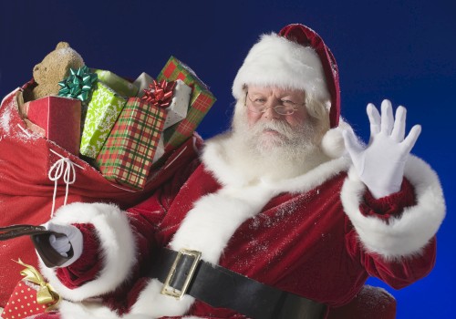 A person dressed as Santa Claus is waving, with a large red sack filled with wrapped gifts and a teddy bear over their shoulder, against a blue background.