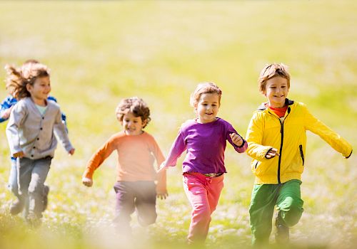 A group of four children is running and playing in a grassy field, enjoying a sunny day.