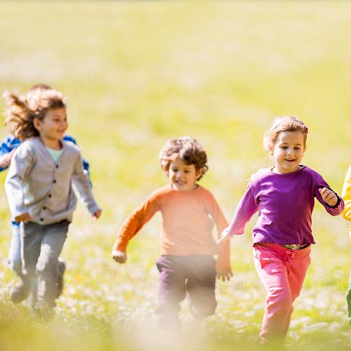 A group of four children is running and playing in a grassy field, enjoying a sunny day.