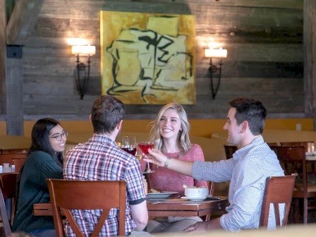 A group of four friends sitting at a restaurant table, laughing and toasting drinks.