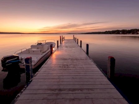 A serene sunset over a calm lake, with a wooden dock extending into the water and a boat moored to the side.