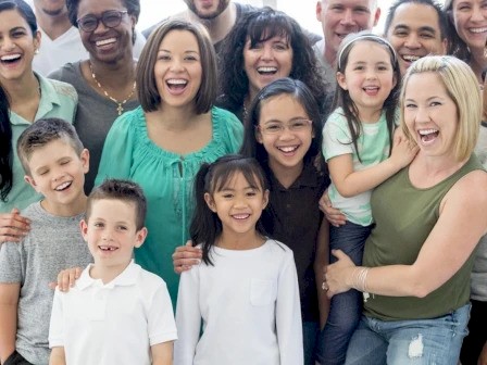 A diverse group of people, including adults and children, smiling and posing together in a cheerful gathering.