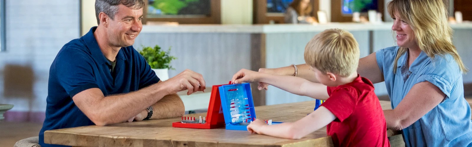 A family of three is gathered around a table playing a board game with smiles, enjoying their time together indoors.