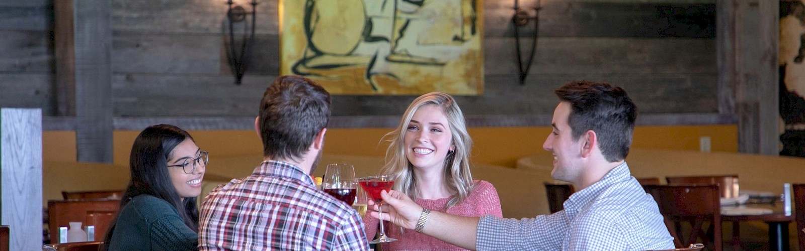 Four people are sitting at a restaurant table, engaging in conversation and raising their glasses for a toast.