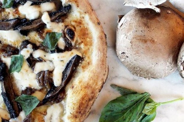 The image shows a mushroom pizza topped with cheese and basil leaves, next to three fresh mushrooms and more basil leaves on a marble surface.
