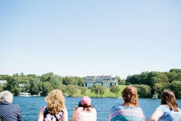 Five people are seen from the back, looking at a large building across a body of water, surrounded by trees and greenery, ending the sentence.
