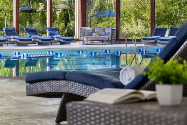 This is an indoor pool area with lounge chairs, a rolled towel, an open book, and a potted plant near a large glass window.